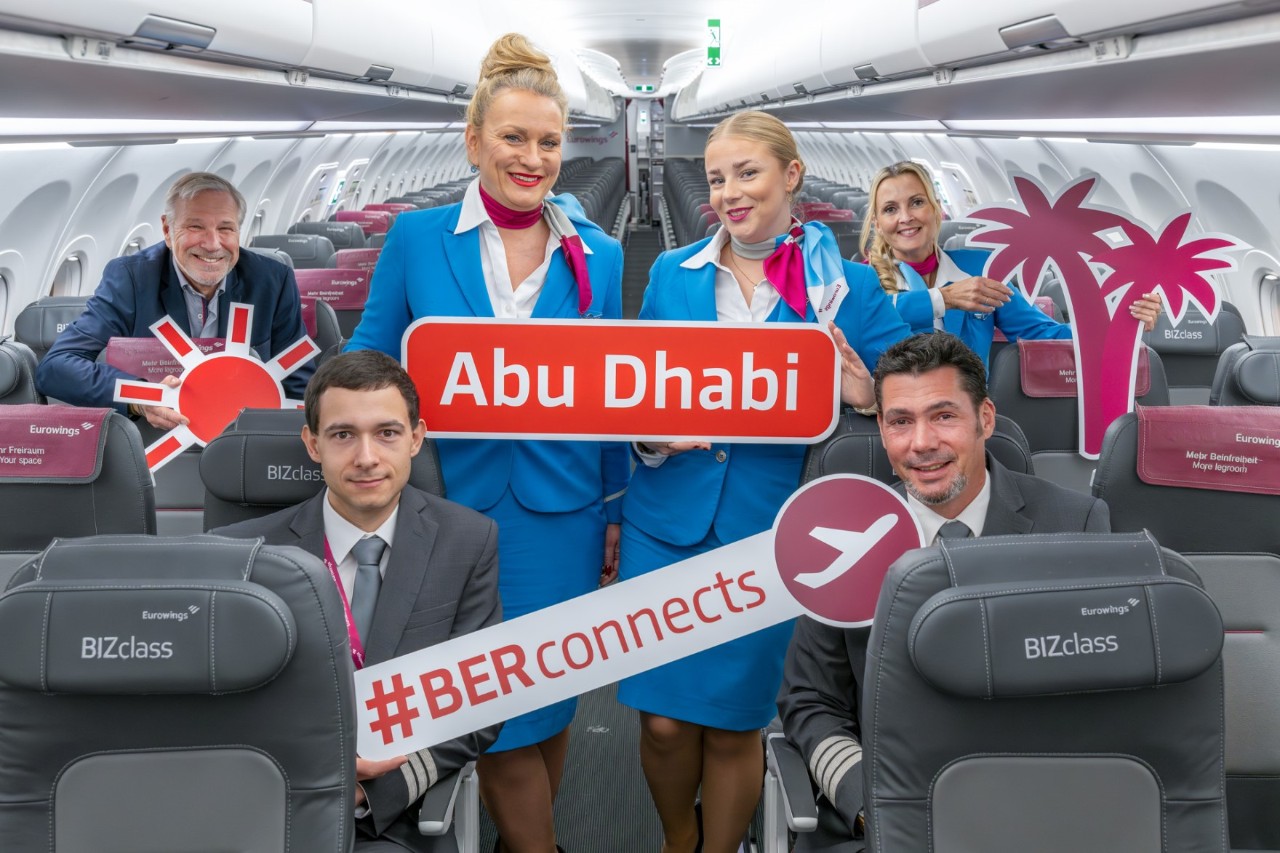 An aircraft crew poses in the aircraft with signs reading Abu Dhabi and #BERconnects.