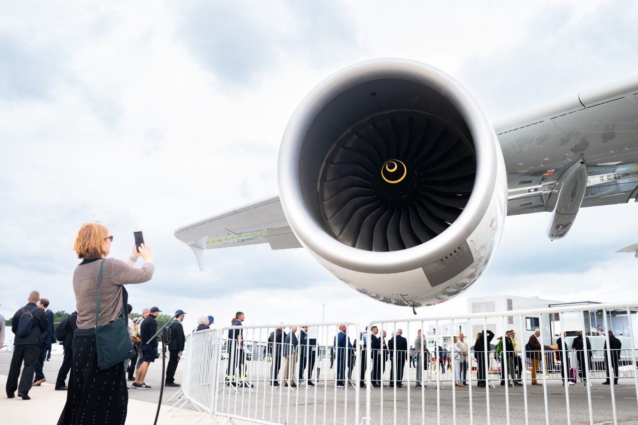 Besucherin fotografiert Flugzeugtriebwerk. Dahinter warten Besucher*innen auf Zutritt zu einem Flugzeug.