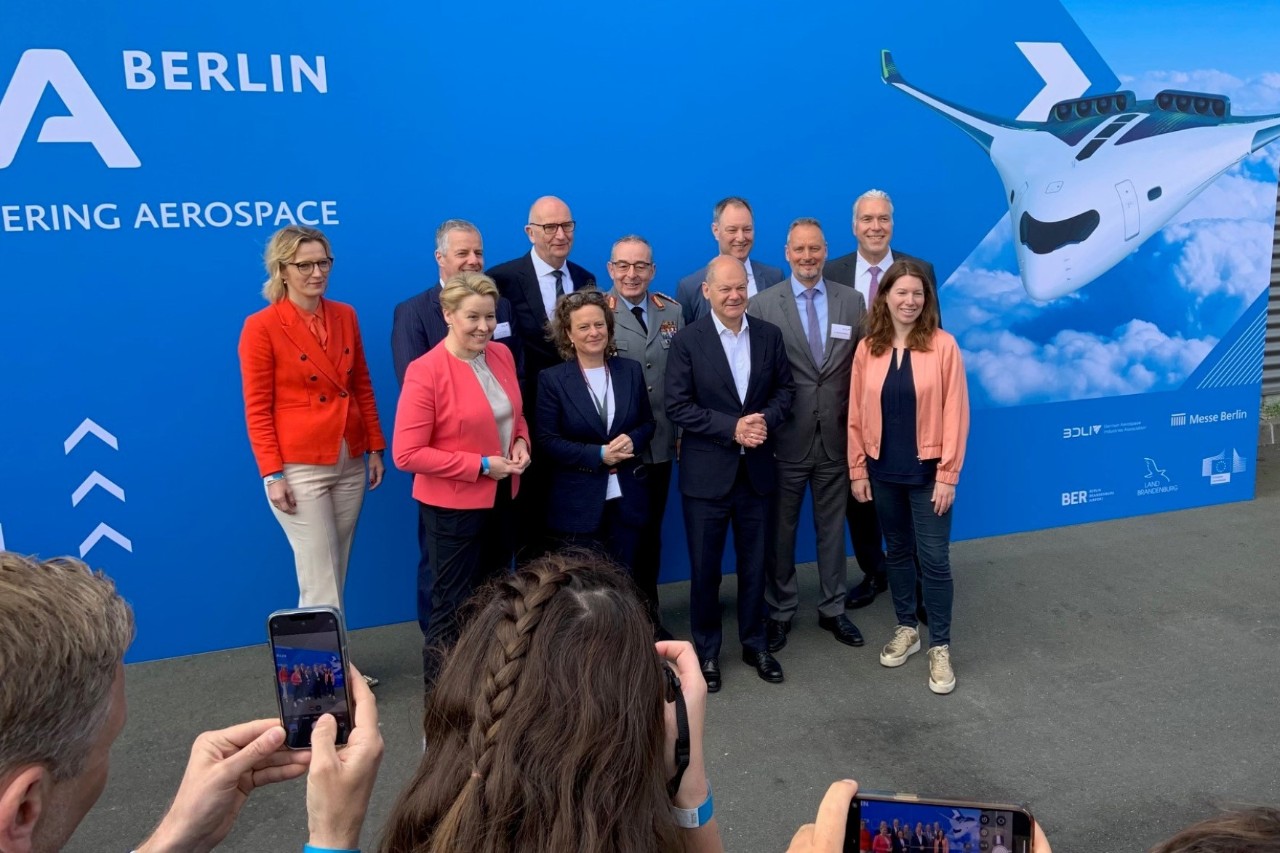 Mehrere Personen werden fotografiert. Im Hintergrund ein Schild mit der Aufschrift ILA Berlin und einem Modellflugzeug.