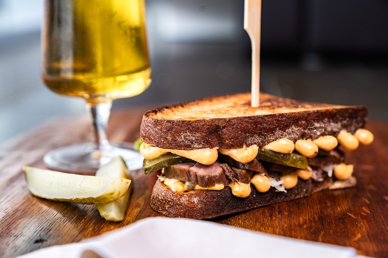 A toasted sandwich, a glass of beer and pickles