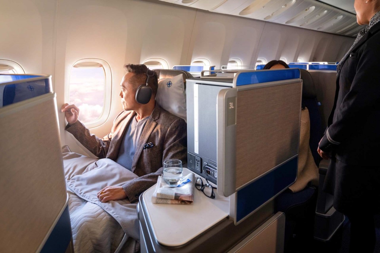 A passenger with a blanket and headphones looks out of an aircraft window