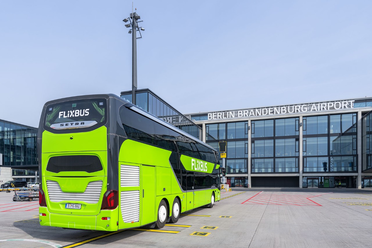 A green long-distance coach is parked in front of the terminal. The long-distance coach is seen from the rear.