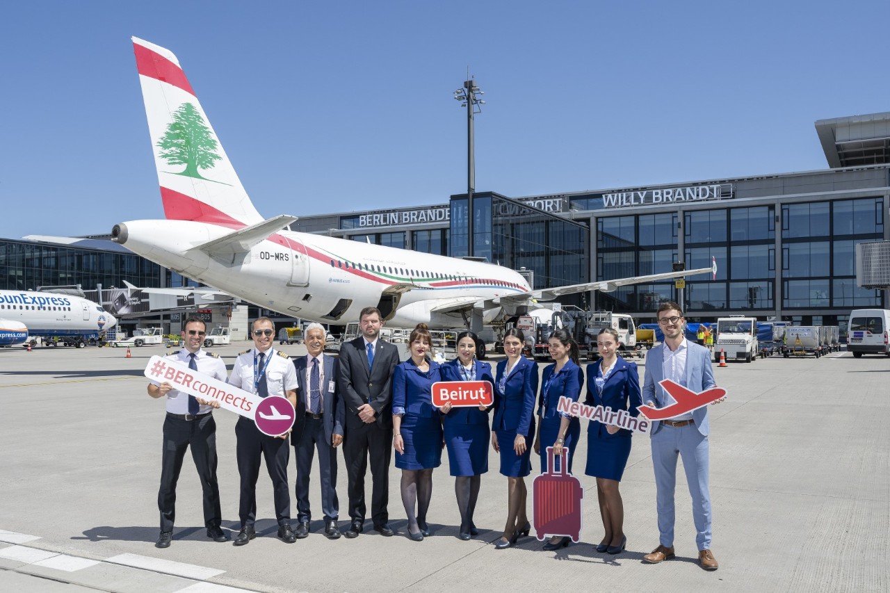 A group of people are standing in front of a Middle East Airlines aeroplane, holding signs and posing for a photo.