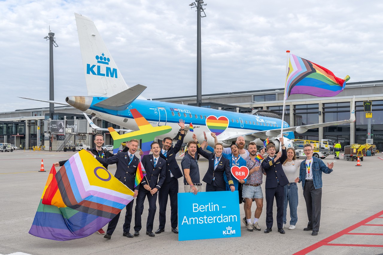 A group of people holding colorful signs and flags in front of a KLM plane at BER