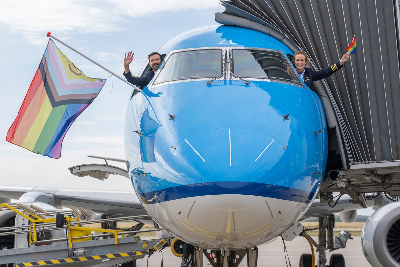 Female and male pilots holding a rainbow flag aboard a KLM aircraft at BER