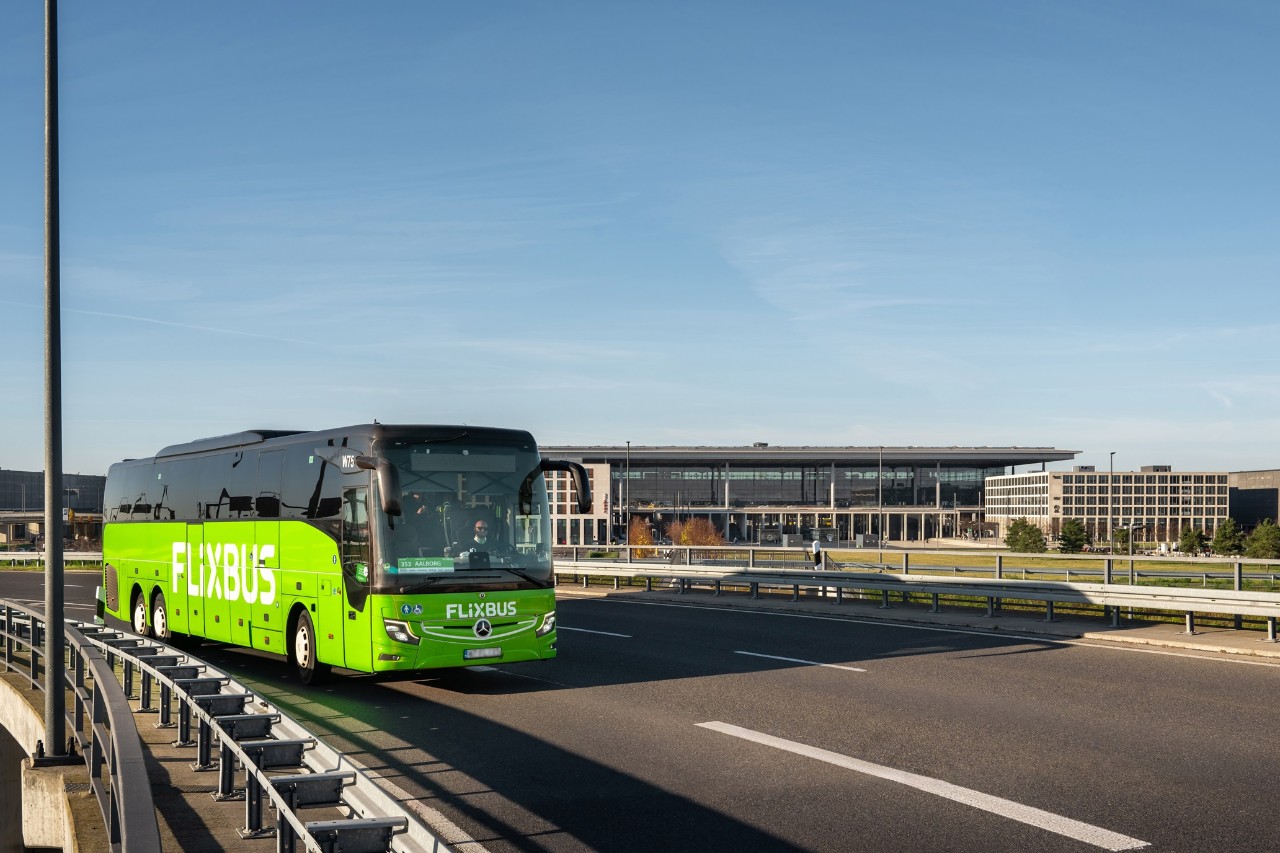 A green coach driving along a highway, with the terminal in the background.
