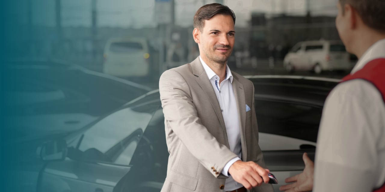 Man hands over his car key to valet employee in front of Terminal 1, informing him that this is a new service that can be booked.