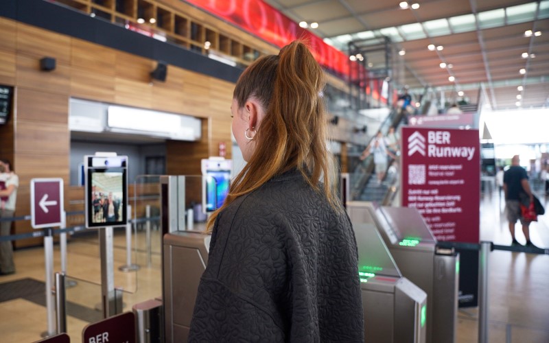 A person stands in the check-in hall of BER Terminal 1 at the entrance to the BER runway security control.