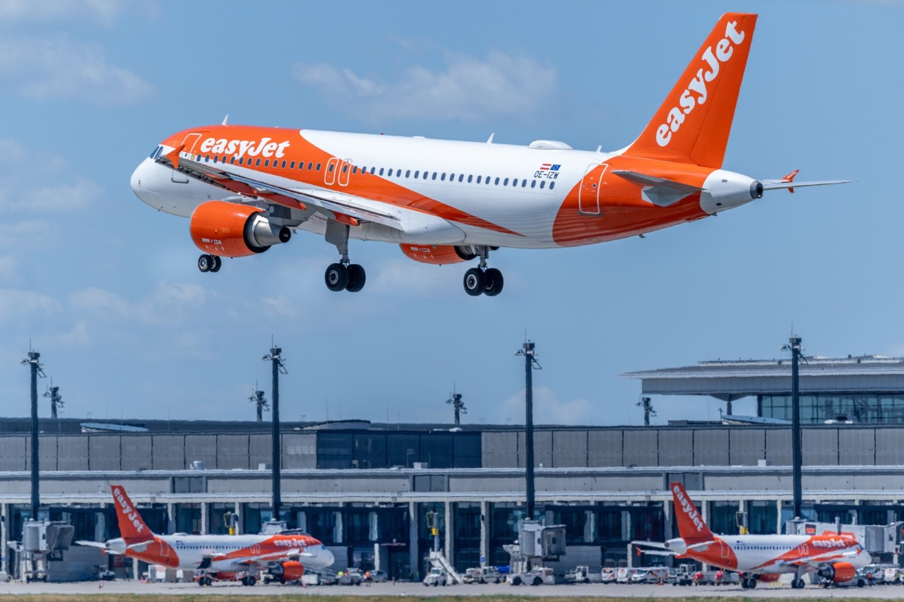 Ein easyJet-Flugzeug kurz vor der Landung. Im Hintergrund ist das Terminalgebäude des BER zu sehen.